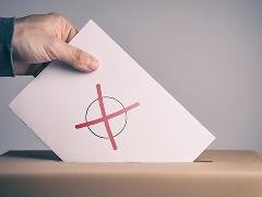 Eine Personal wirft Wahlunterlagen in eine Wahlurne