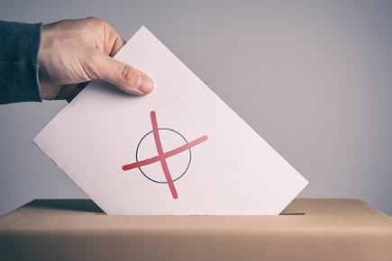 Eine Personal wirft Wahlunterlagen in eine Wahlurne